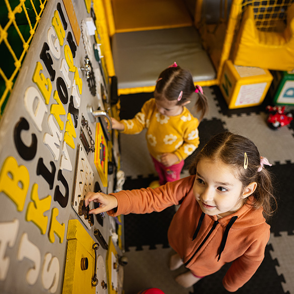 two sisters playing with a busy board at STEAM children's museum